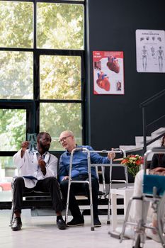 Practitioner medic looking at medical radiography with senior injured patient while discussing diagnosis expertise during checkup visit appointment in hospital waiting area. Health care service