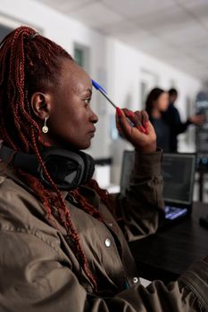 Pensive african american developer brainstorming ideas while typing code and create new interface in data room. Engineer programming server database in busy artificial intelligence developing agency.