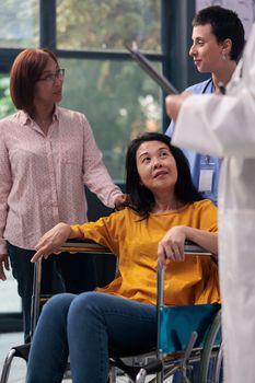 Senior physician talking to wheelchair user and consulting injured patient sitting in hospital waiting area. Doctor giving support and advice to patient with disease, checkup visit. Medicine concept