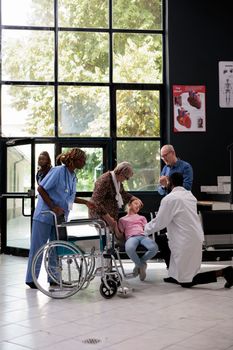 Grandparents being worried after exhausted granddaughter falling down on chair in hospital waiting room during consultation. Medic consulting unconscious little child before putting medical expertise