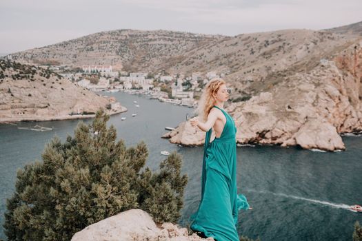 Close up shot of beautiful young caucasian woman with curly blond hair and freckles looking at camera and smiling. Cute woman portrait in a pink long dress posing on a volcanic rock high above the sea