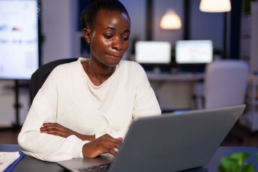 Overworked african american businesswoman reading business email on laptop computer overworking in startup company office. Black manager typing management strategy. Marketing statistics