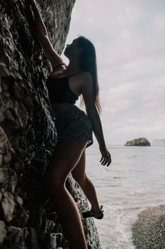A girl climbs a rock. The athlete trains in nature. Woman overcomes difficult climbing route. Extreme hobby. Tourist woman rock climber hiking on mountains rocks over beautiful sea coast