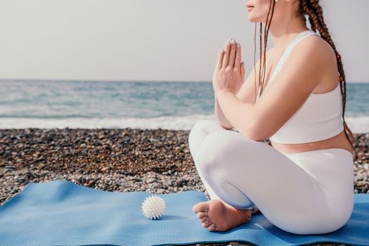 Woman yoga sea. Young woman with braids dreadlocks in white swimsuit and boho style braclets practicing outdoors on yoga mat by the ocean on sunny day. Women's yoga fitness routine. Healthy lifestyle, harmony