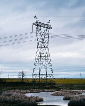 High voltage post or High voltage tower in the countryside with a small lake. Cloudy background.