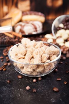 Brown sugar in a glass bowl next to candies and sweets on dark vintage wooden background