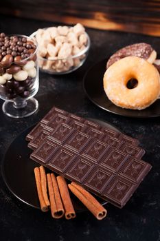 Top view of chocolate tablets, donuts, brown sugar with peanuts in chocolate and coffee beans on dark vintage wooden background