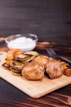 Grilled chicken next to fried zucchini and sweet potatoes on wooden background