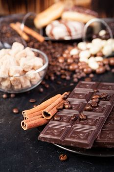 Chocolate tablets next to cinnamon rolls and other sweets and candies on a wooden background