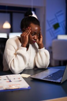 Exhausted african american businesswoman massage forehead having headache pain suffering from migraine. workaholic Tired black entrepreneur working at company strategy late at night in office