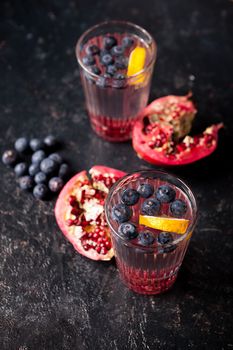 Two glasses with infused water with organic berries and pomegranate on vintage wooden dark background