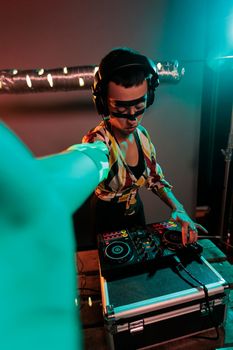 Female DJ with cool makeup mixing techno music, using turntables to produce remix of record in studio with colorful lights. Disc jockey performing at club with stereo and audio equipment.