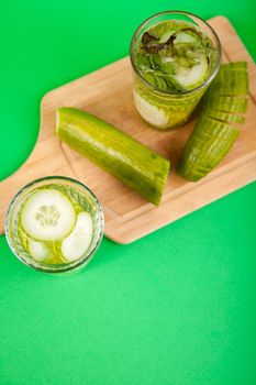 Homemade detox water from organic cucumbers in a glass against a green background
