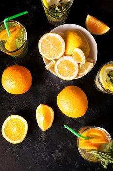 Top view of healthy and delicious lemonade and orangeade next to cutted fruits on dark vintage wooden board