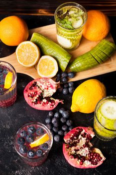 Top view of fruits, vegetables and berries next to glasses with detox water on dark wooden background