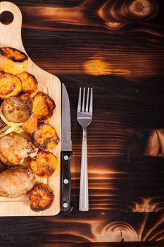 Top view of wooden board with homemade fried chicken next to grilled vegetables on wooden background