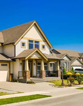 A perfect neighborhood. Big family house with concrete driveway to the garage. Residential house with door steps and porch over entrance on blue sky background