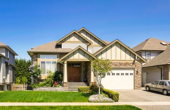 A perfect neighborhood. Luxury family house with car parked on concrete driveway. Residential house with landscaped front yard on blue sky background