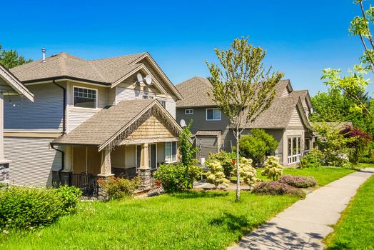 A perfect neighborhood. Concrete pathway along the row of residential houses on a sunny day with blue sky background