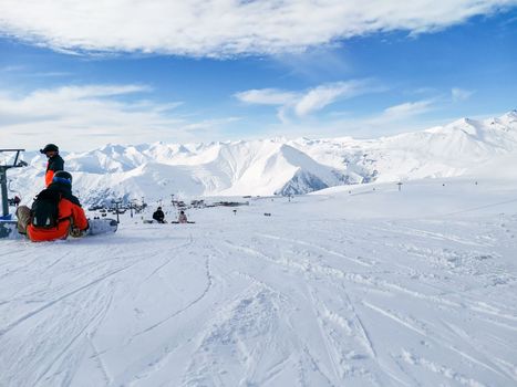 Ski slope. Snowboarder sits on snow. Winter sport. Ski resort of Georgia Gudauri. Snowy slope and mountains