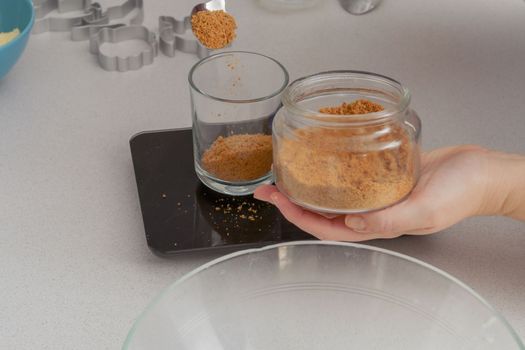 glass jar with brown sugar and a spoon in the background the hands of a woman preparing a cake