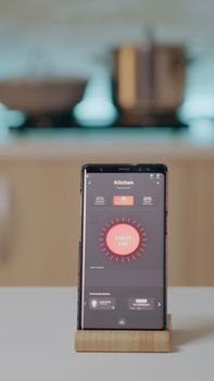 Mobile phone with wireless lighting automation software placed on kitchen desk in empty house with smart system, turning on lights. Smartphone with high tech app controlling electricity effiency