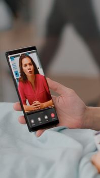 Sick patient resting in bed with mother greeting remote friend during online videocall conference meeting during recovery examination. Little daughter suffering medical surgery in hospital ward