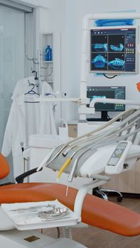 Revealing shot of orthodontic chair with nobody in, teeth x ray images on modern display. Empty medical clinic stomatology hospital room with dentistry equipment, ready for dental heath treatment