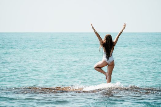 Young woman in swimsuit with long hair practicing stretching outdoors on yoga mat by the sea on a sunny day. Women's yoga fitness pilates routine. Healthy lifestyle, harmony and meditation concept.