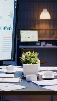 Modern empty business corporate office meeting room is ready for businesspeople late at night. In background on conference table standing company financial documents with economy graphs