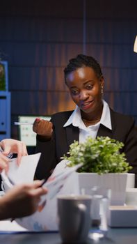 African american focused entrepreneur brainstorming business company strategy working ovetime in meeting room in evening. Diverse multi ethnic coworkers analyzing management presentation paperwork