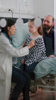 Paediatric woman doctor consulting sick patient listening heartbeat using medical stethoscope in hopsital ward. Father support hospitalized daughter wearing nasal tube during medical appointment