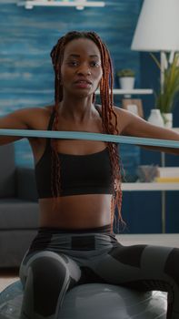 Trainer slim black woman recoring online yoga training using videocamera during morning fitness workout in living room. Fit athletic doing body exercices using aerobic elastic