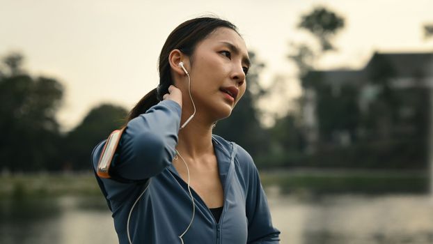 Beautiful athlete woman resting after running outdoor, standing near lake and mountains sunny landscape on background.