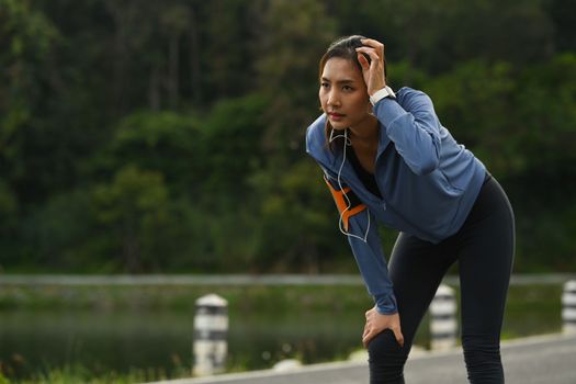 Tired athletic woman in sportswear taking break, resting after running in the park. Healthy lifestyle, workout and wellness concept.