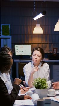 Businesswoman leder sitting at desk analyzing marketing presentation discussing financial graps paperwork. Diverse multi-ethnic teamwork brainstorming project ideas working in meeting room late night