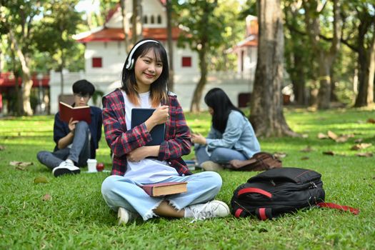 Pretty asian students woman in wireless headphone while sitting on campus lawn. Education and lifestyle concept.