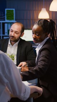 Multi ethnic business team sitting at conference table in office meeting room checking financial graphs presentation overworking at management project. Diverse coworkers brainstorming company ideas