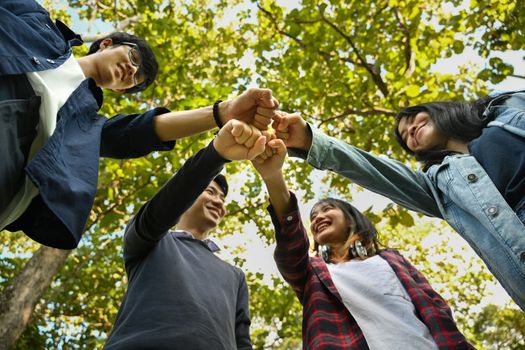 Low angle view of four university students join hand together. University, youth lifestyle and friendship concept.