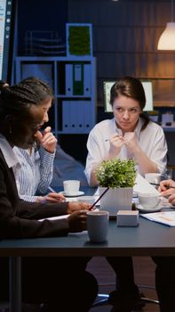 Diverse multiethnic business teamwork overworking in office meeting room analyzing financial graphs paperwork late at night. Coworkers brainstorming project ideas solving company problem