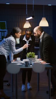 Focused leader woman enter in office meeting room lean on conference table brainstorming business company presentation late at night. Diverse multi ethnic teamwork solving management strategy