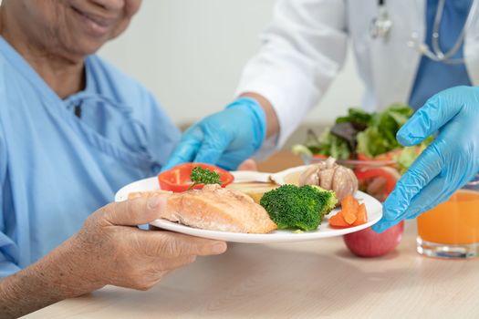 Asian senior old lady woman patient eating breakfast and vegetable healthy food with hope and happy while sitting and hungry on bed in hospital.