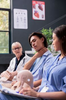 Asian patient need to remove neck collar while receiving help from medical staff during consultation in hospital waiting area. Young adult wearing cervical brace to recover after accident injury