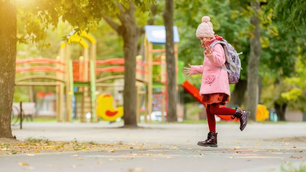 School girl with backpack playing outdoors at autumn park after lessons. Pretty child kid walking at street