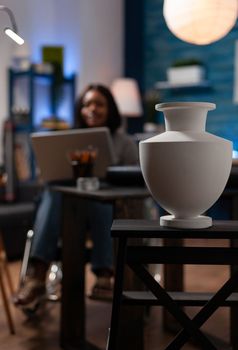 Female person with artistic skills using wheelchair to move around, reviewing online drawing techniques from laptop in home art studio. African american creating vase digital artwork on computer.