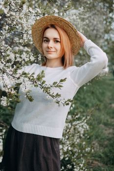 Portrait of a woman in a straw hat in a cherry blossom. Free outdoor recreation, spring blooming garden