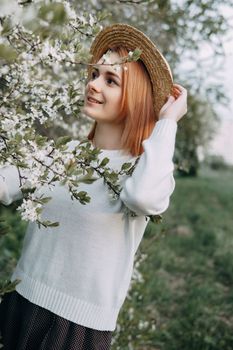 Portrait of a woman in a straw hat in a cherry blossom. Free outdoor recreation, spring blooming garden