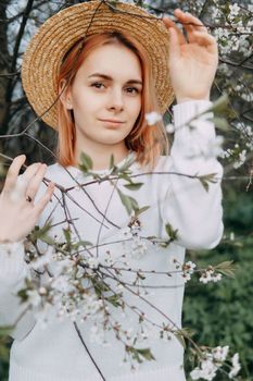 Portrait of a woman in a straw hat in a cherry blossom. Free outdoor recreation, spring blooming garden