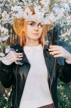 Portrait of a woman in a straw hat in a cherry blossom. Free outdoor recreation, spring blooming garden.