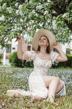 An attractive long-haired woman walks in the spring in the park of blooming apple trees. Spring portrait of a woman